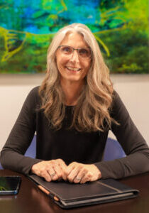 A women with long grey hair and glasses sitting at a conference table